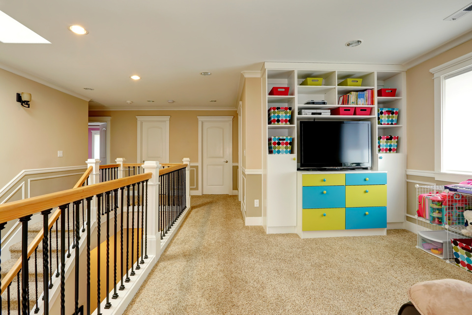 Upper level of modern house furnished with built-in cabinets, tv, storage units. View of staircase and railings
