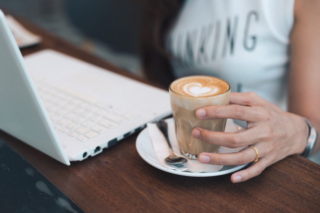 woman hand holding coffee latte with laptop on the wood desk vintage color